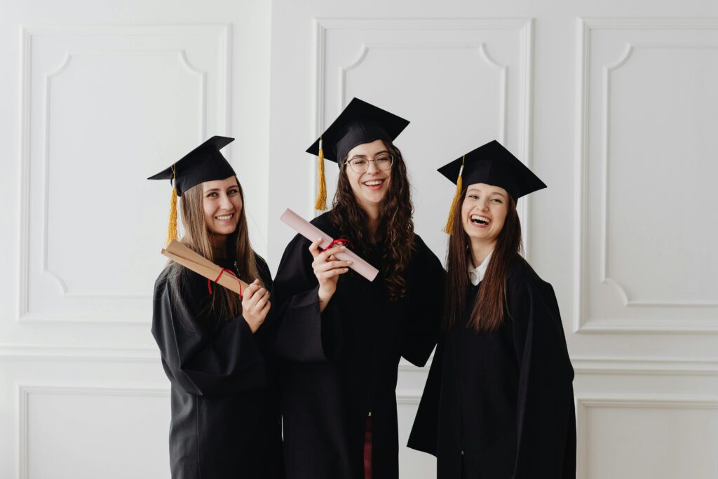 pexels-photo-8106665-8106665 Three happy female graduates in caps and gowns holding diplomas and celebrating their achievement.